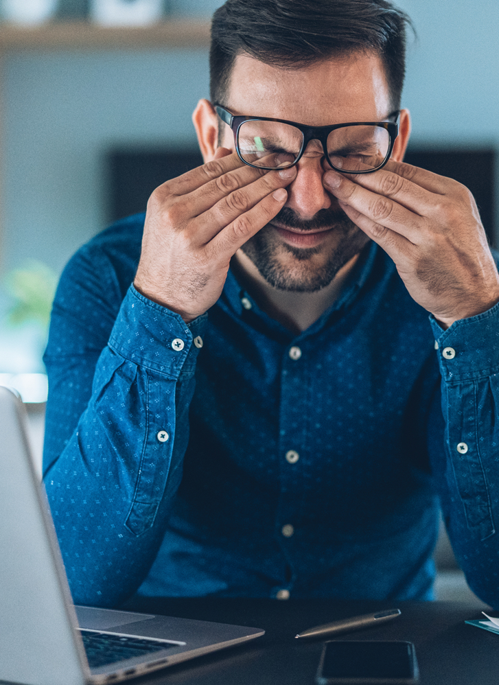 man rubbing eyes at computer desk looking stressed out